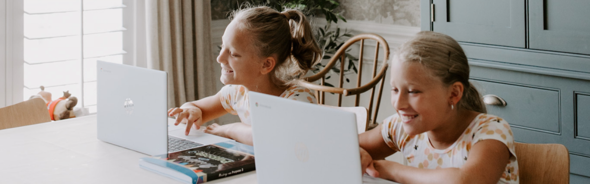 Two girls at home using laptops with Abeka curriculum