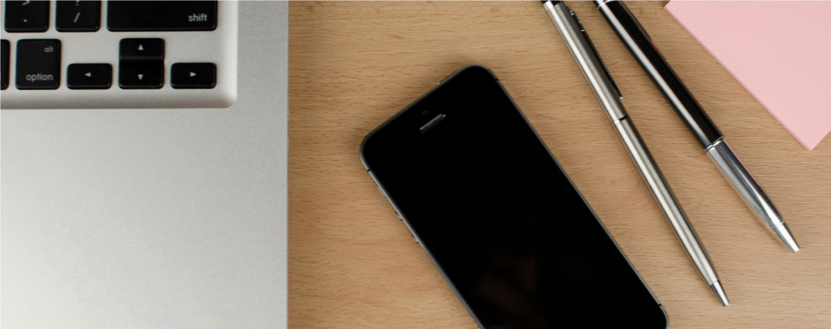 phone and laptop on desk next to writing utensils