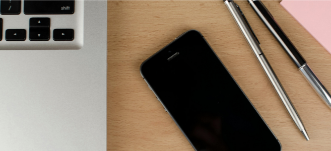 phone and laptop on desk next to writing utensils