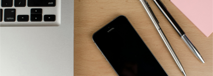 phone and laptop on desk next to writing utensils